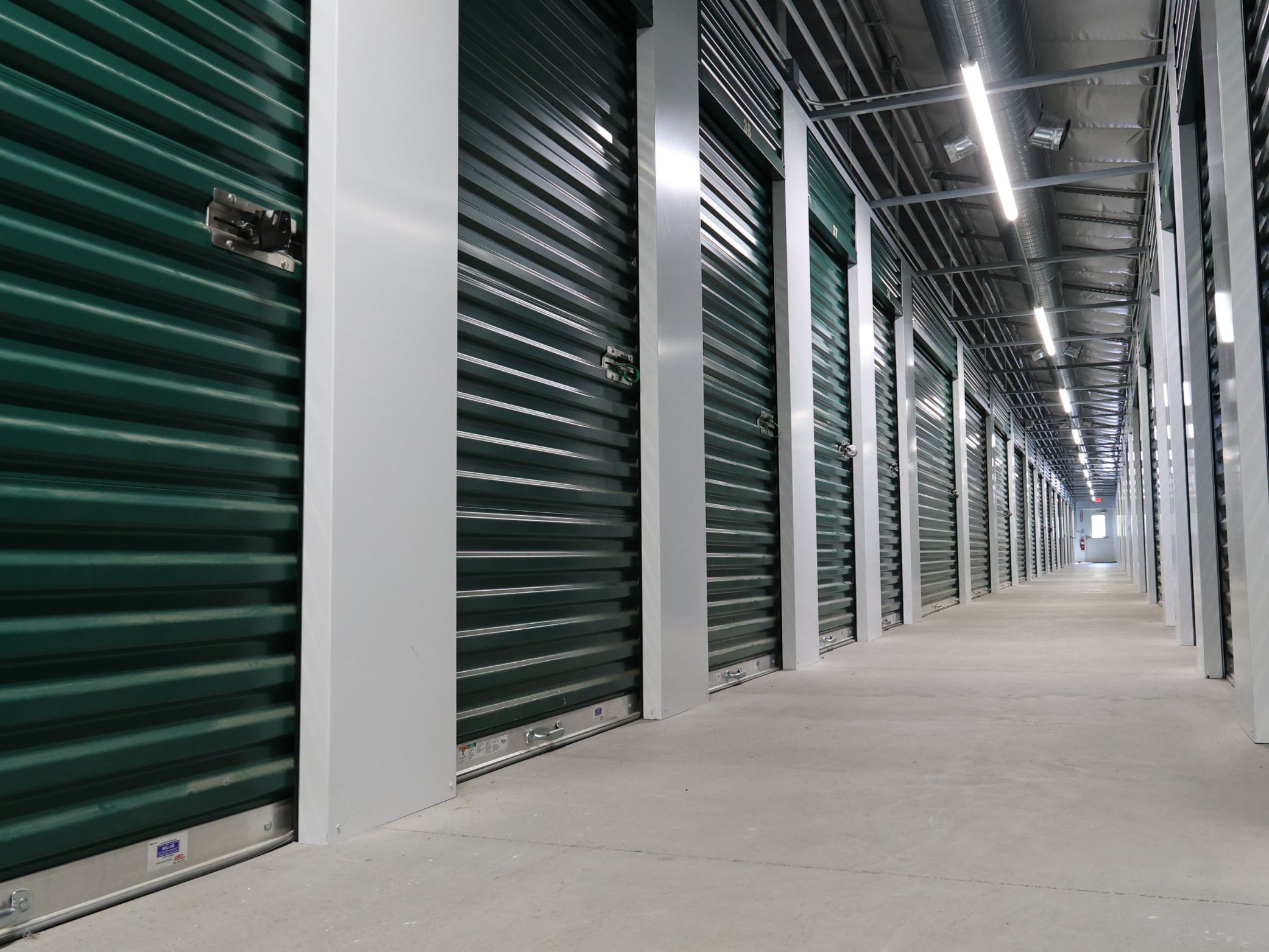 Interior hallway of A-Verdi Self Storage with green storage unit doors, bright overhead lighting, and clean concrete flooring.